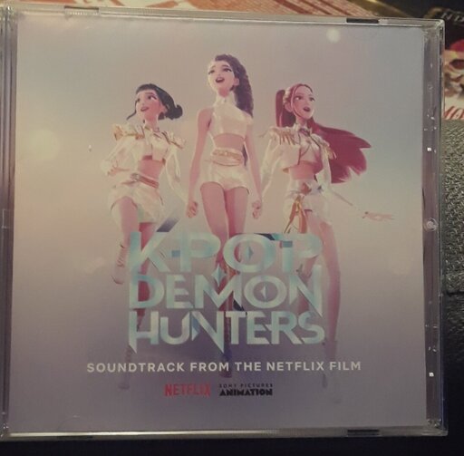 On the CD's front, and in the middle, Zoey, Rumi, and Mira from the film Kpop Demon Hunters are shown. Below them is the words "KPop Demon Hunters Soundtrack from the Netflix film." Below that are the words "Netflix" and "Sony Picures Animation."